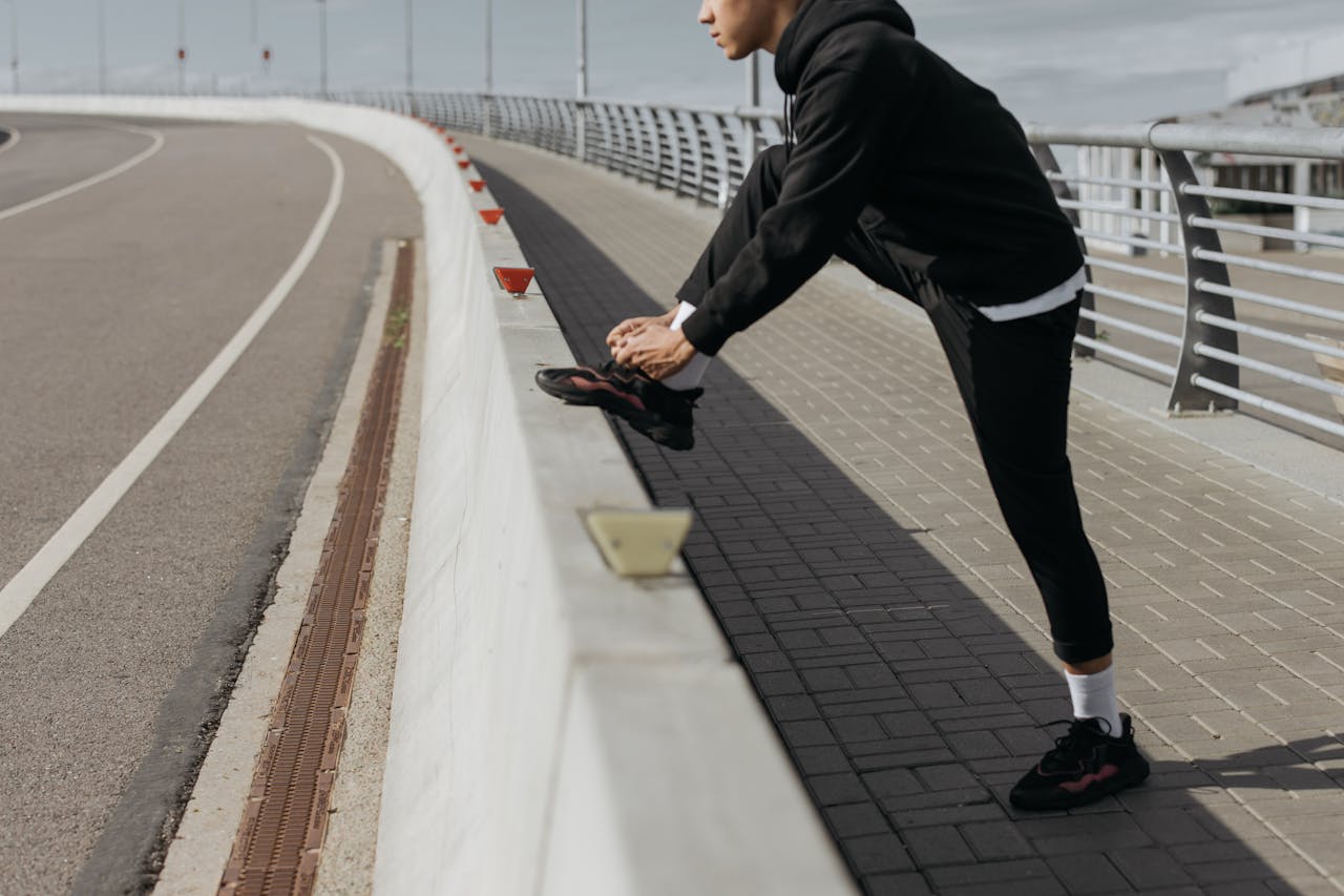services-02 Person in athletic wear stretches on a bridge, preparing for exercise in an urban setting.