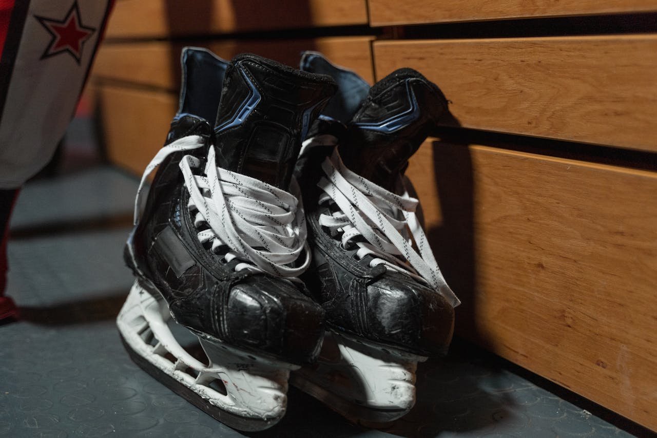 who-we-are A pair of used ice hockey skates lie on the floor in a locker room, showcasing sports equipment.